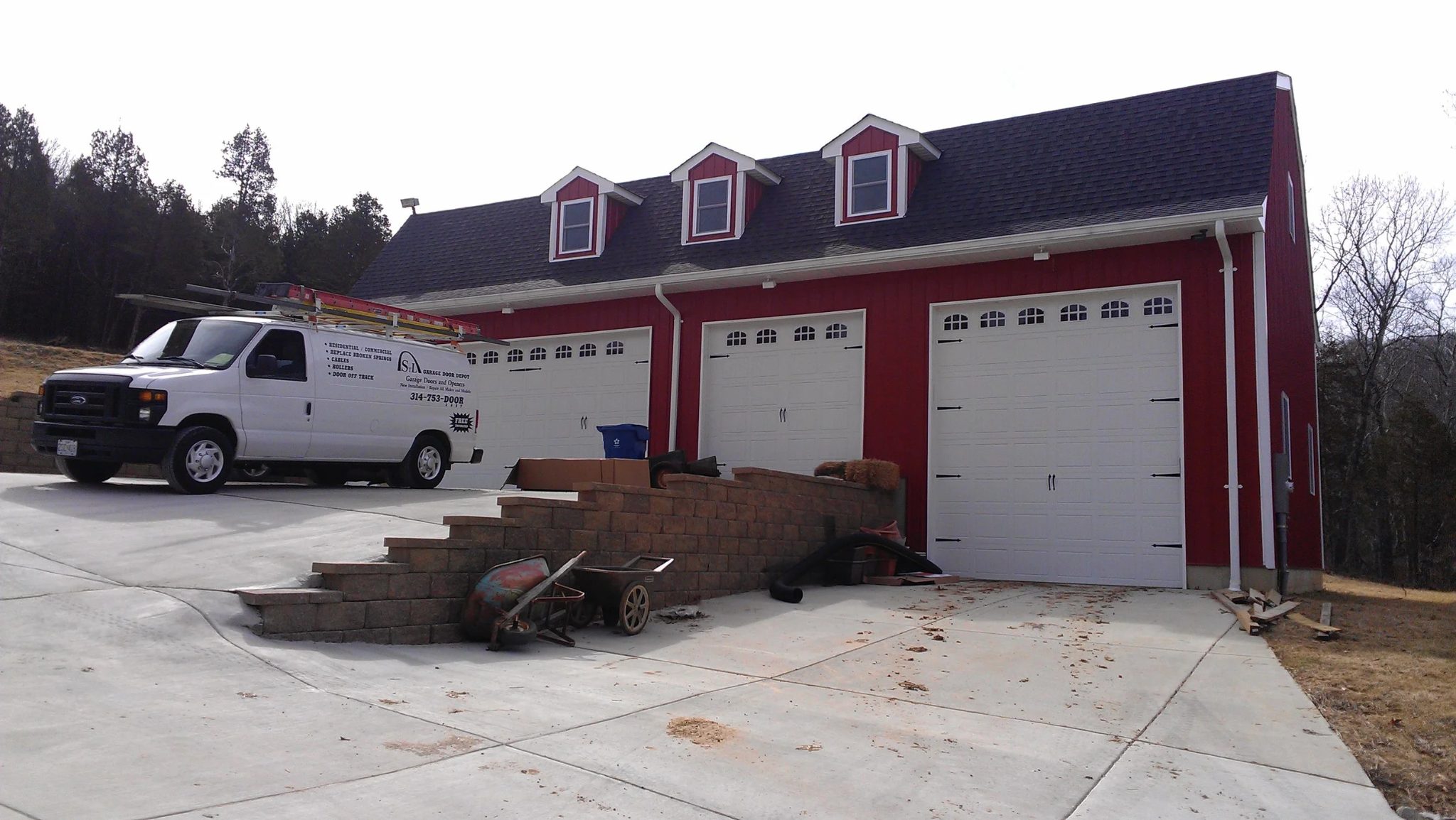 Red barn-style outbuilding with three white sectional garage doors and service van