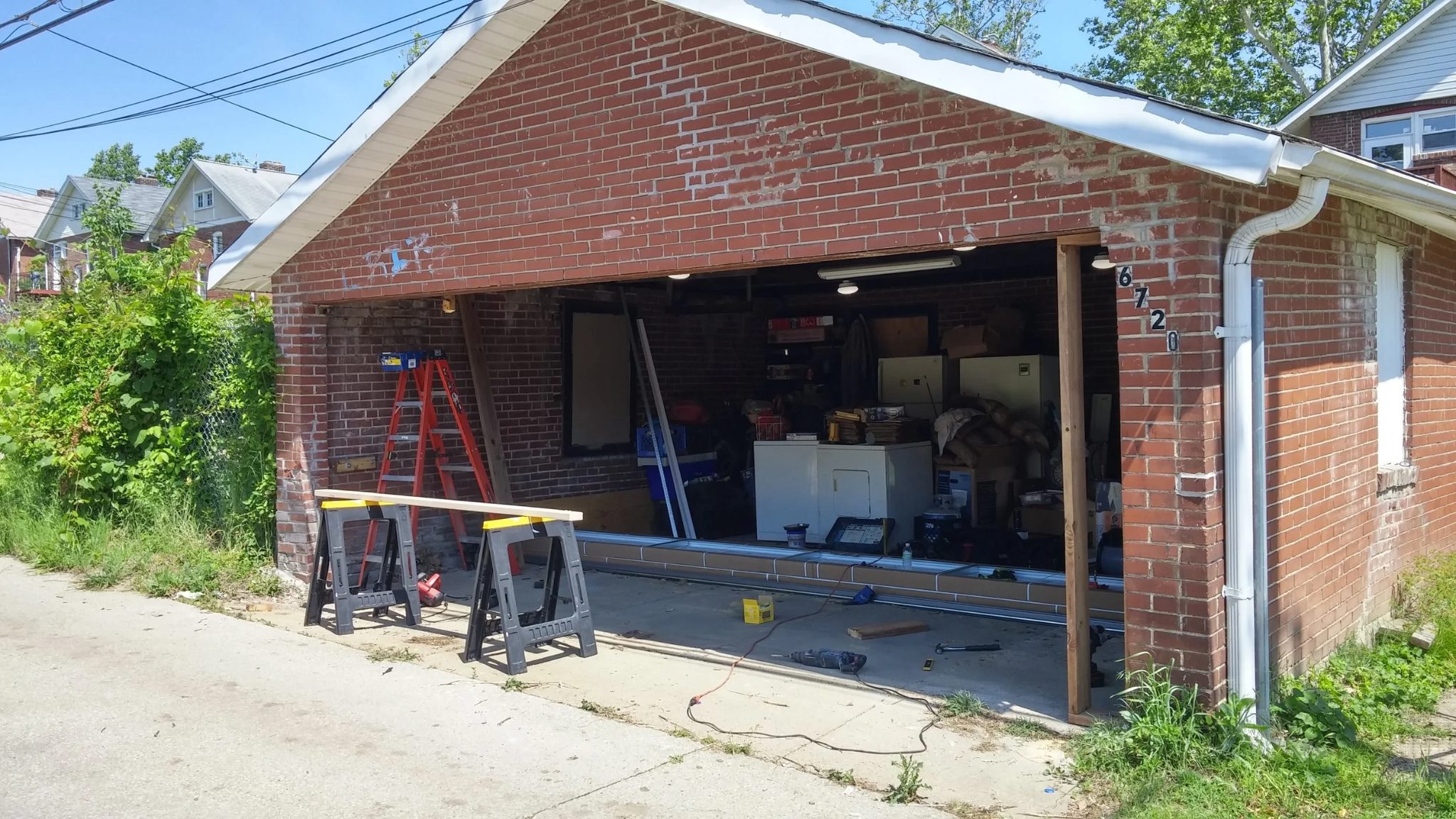 Rough brick garage opening after old door removal, tools and saw horses on site