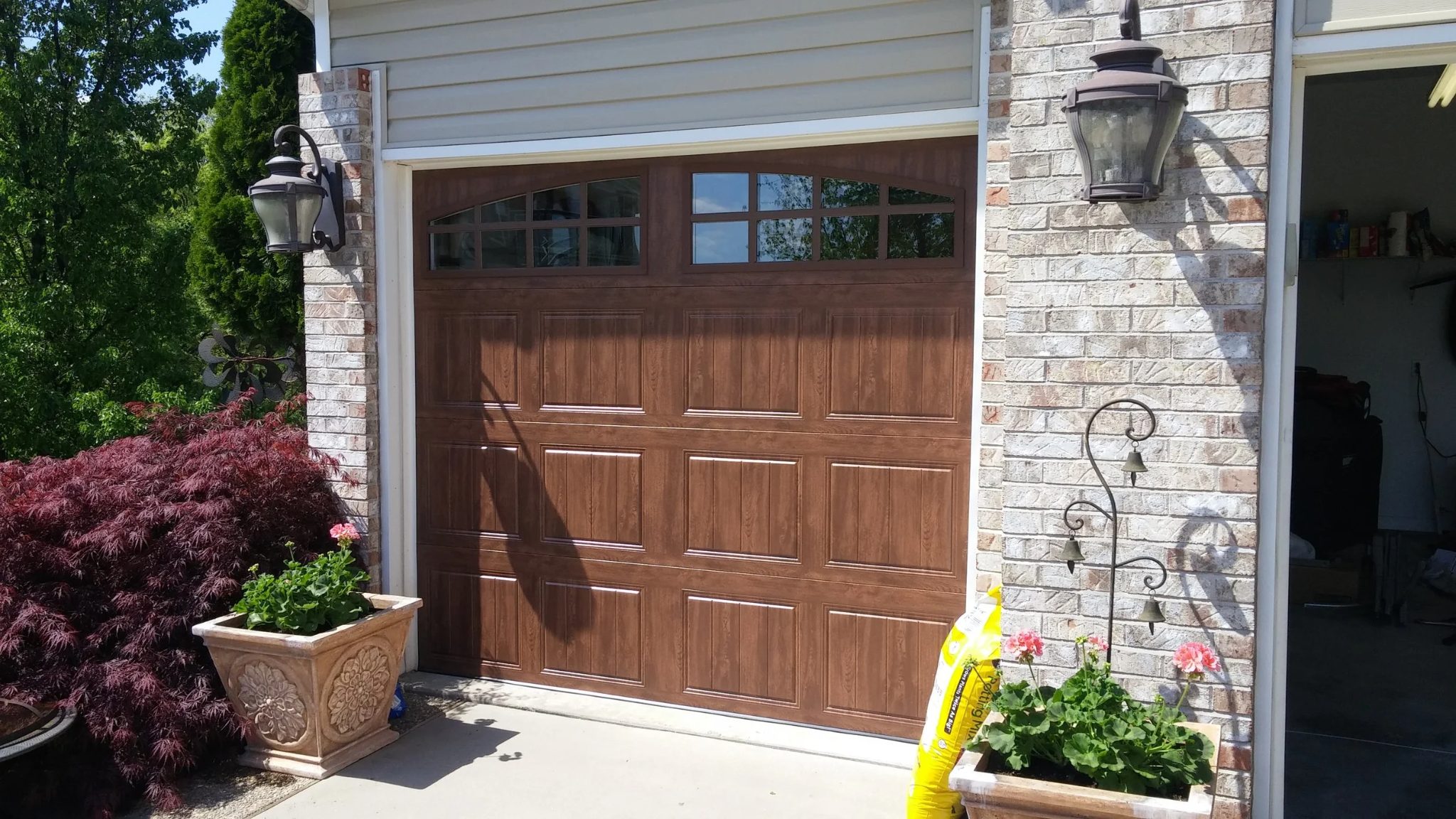 Wood-grain residential garage door with arched windows on a brick home